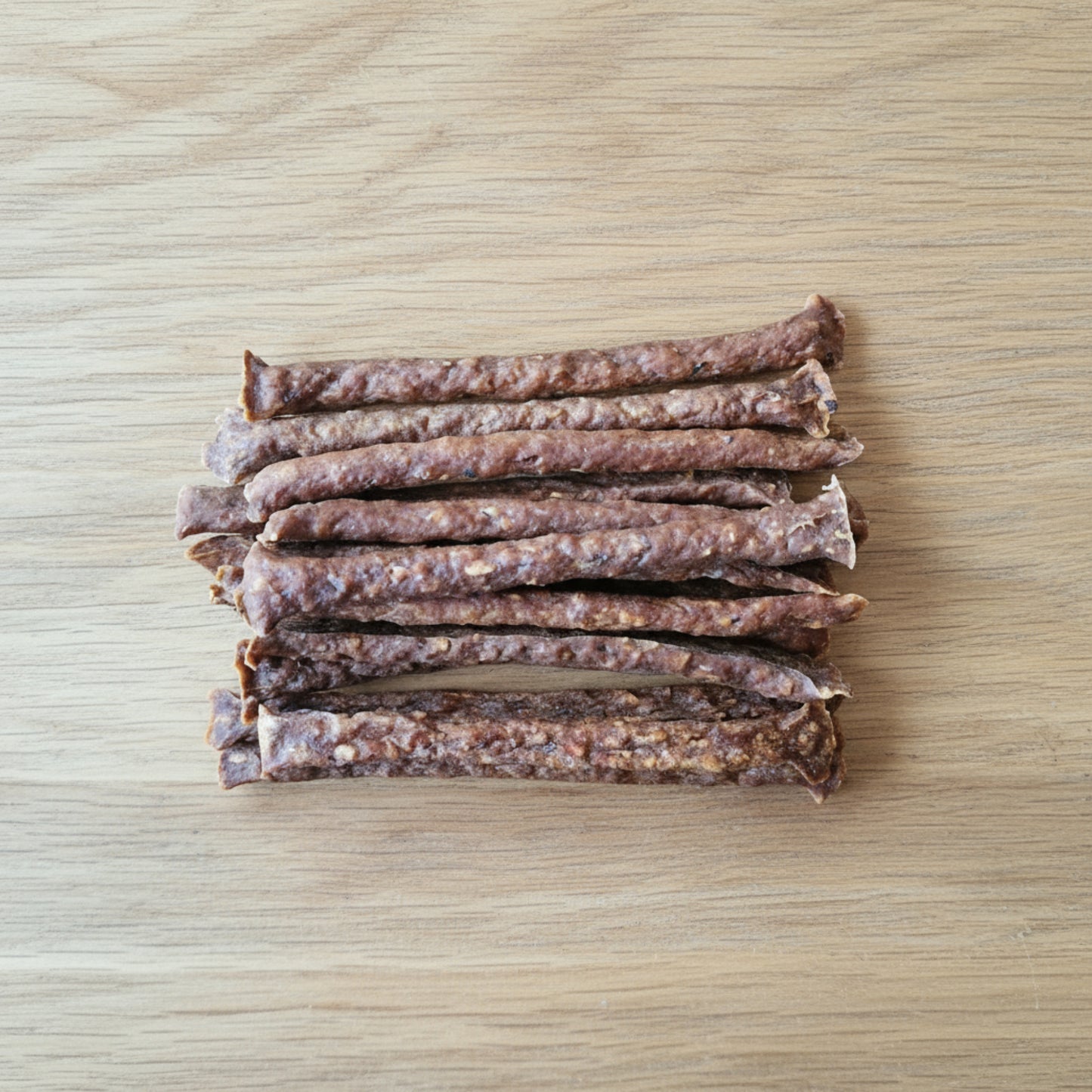 Stack of 15 dried kangaroo muscle meat sticks on a wooden surface