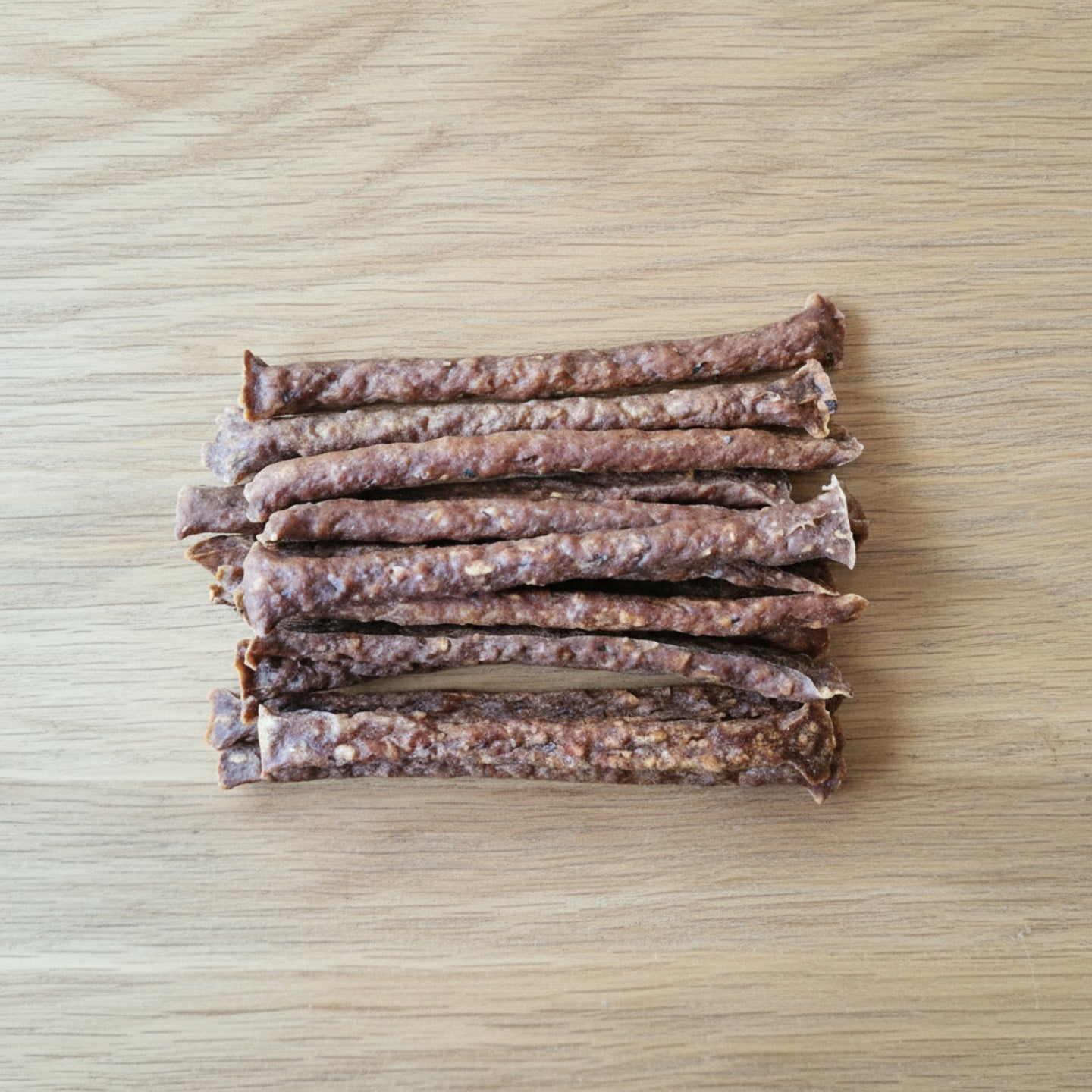 Stack of 15 dried kangaroo muscle meat sticks on a wooden surface